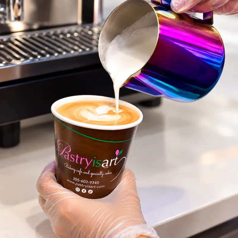 A barista pouring steamed milk into a latte in a Pastry is Art cup